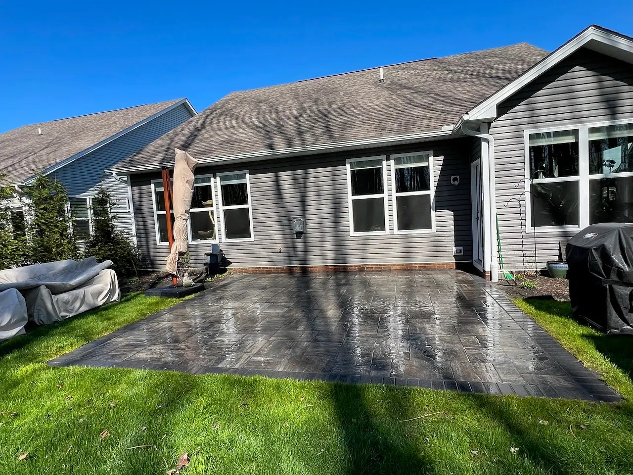 Newly cleaned paver patio behind a gray-sided home with a wet, glossy finish