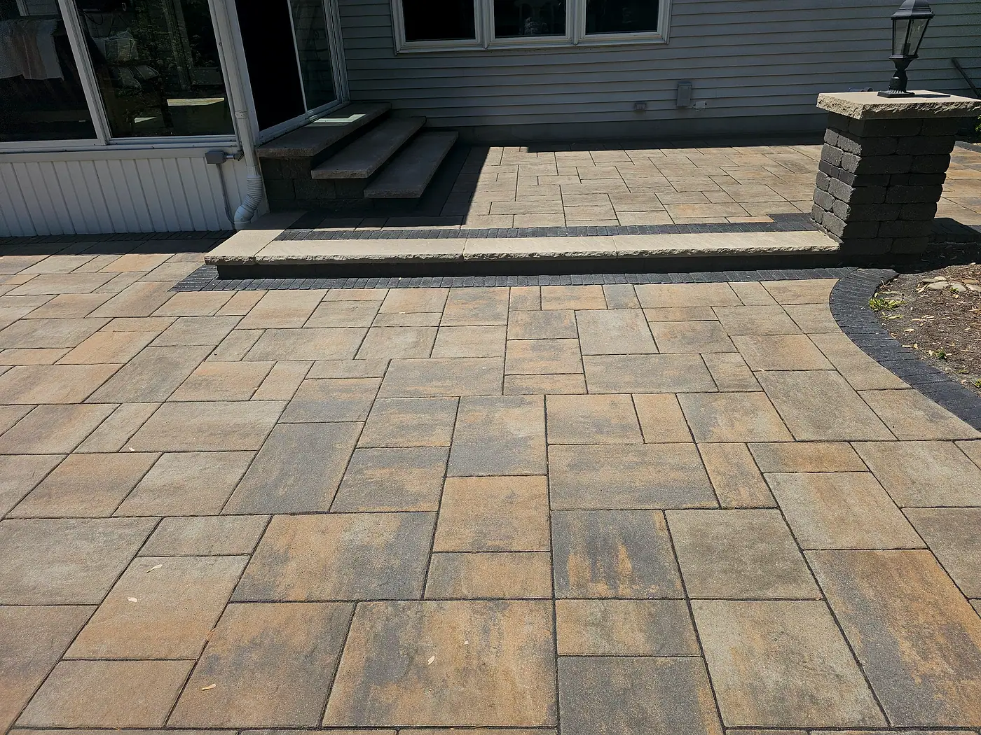 Clean interlocking paver patio with steps leading to the back door