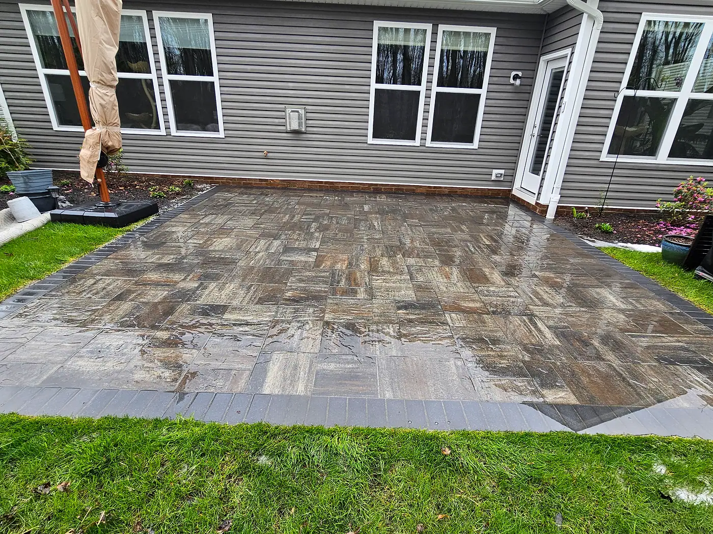 Large paver patio behind a gray home, partly cleaned