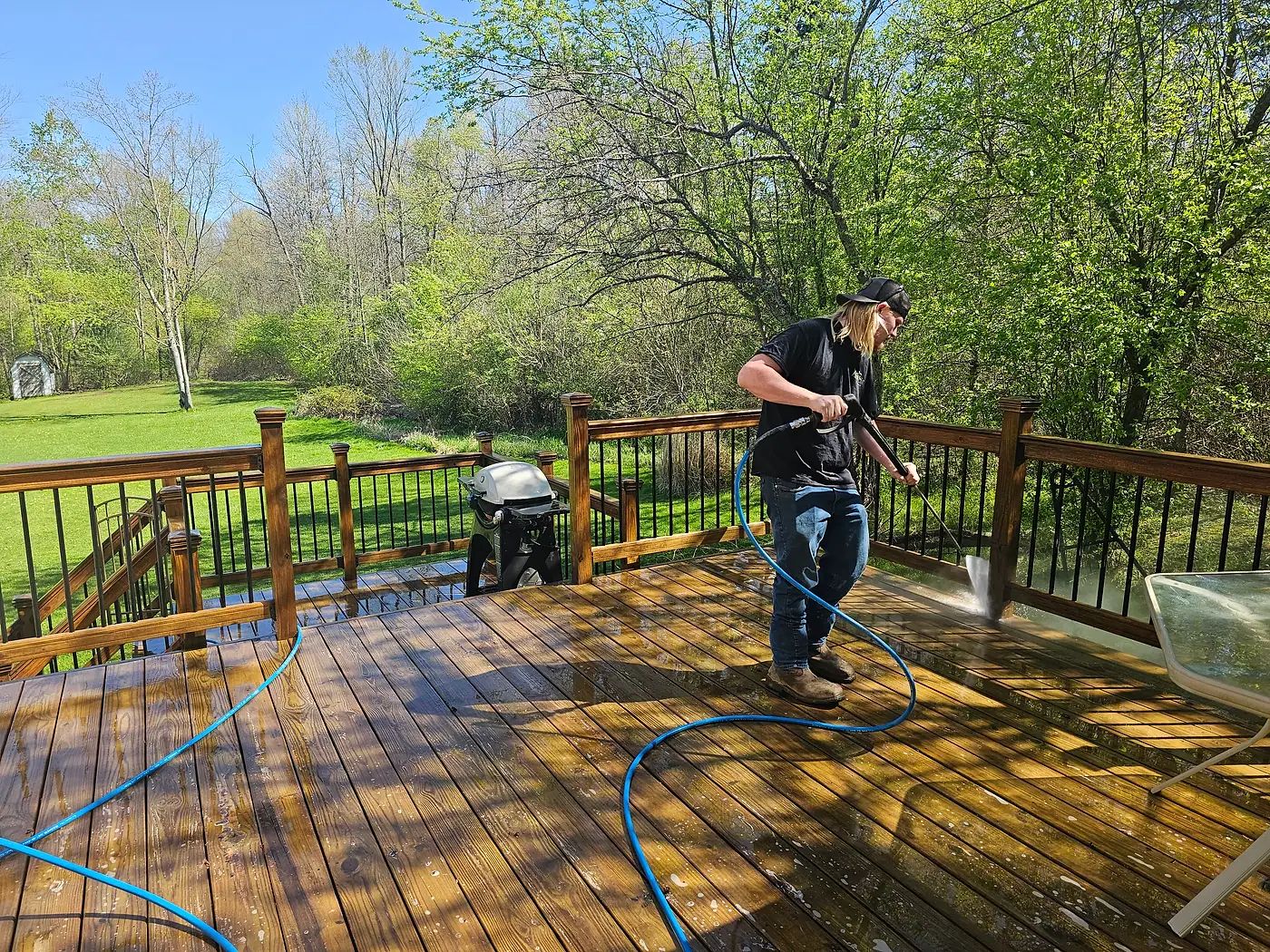 Worker pressure washing a stained wood deck with a blue hose beside the railing