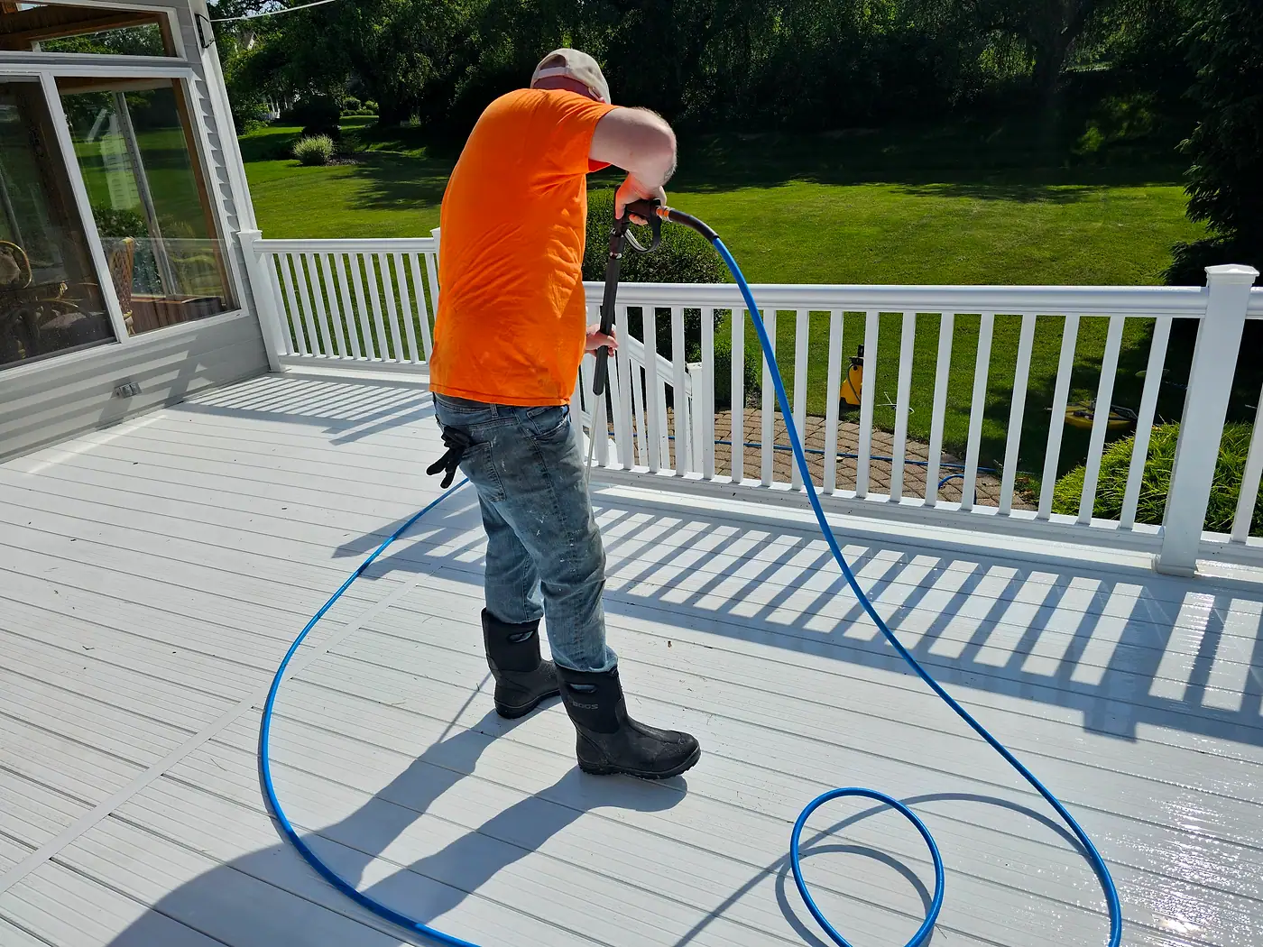 Worker washing a white composite deck beside a white railing
