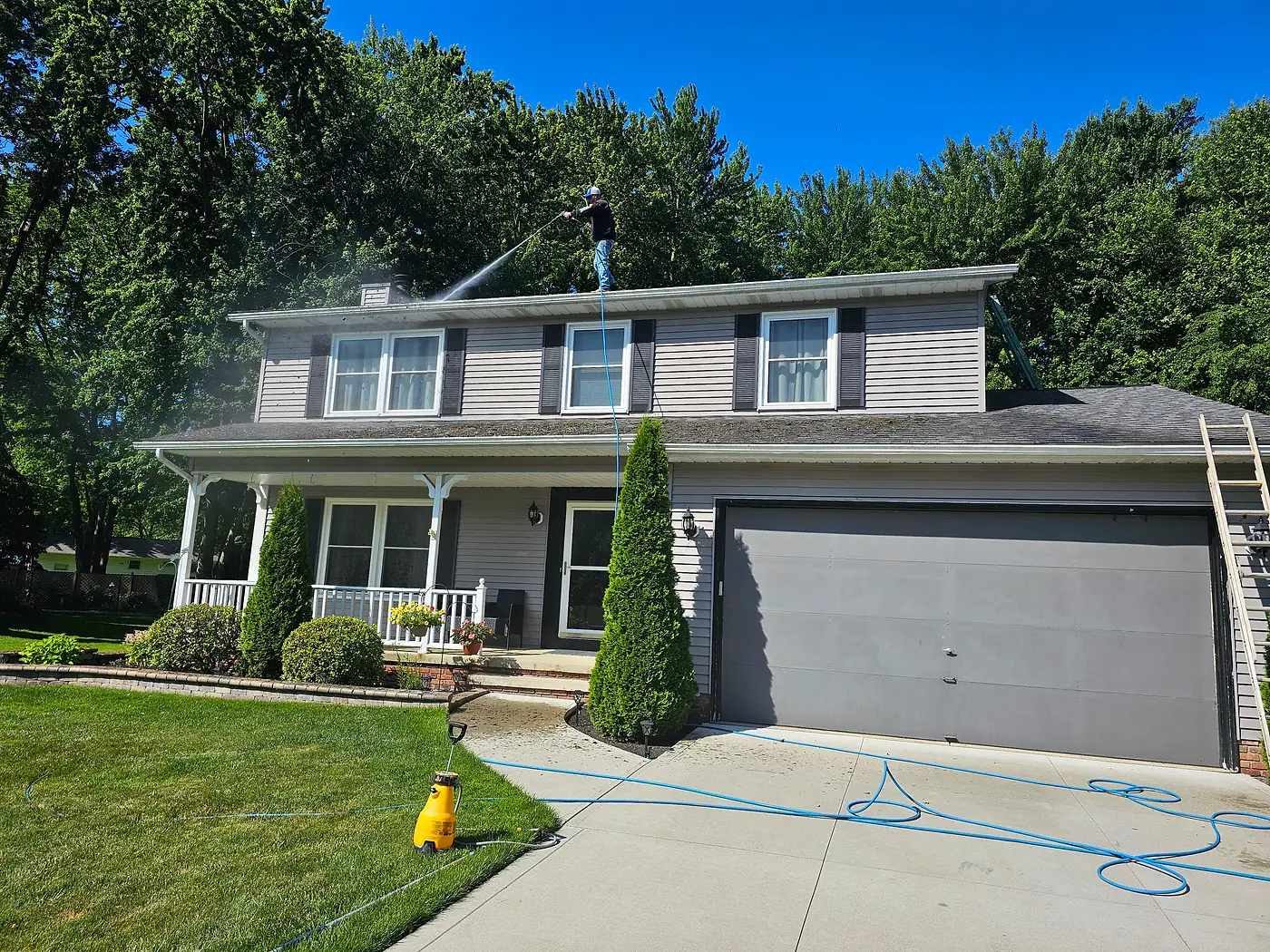Two-story house with a gray garage and a hose laid out on the driveway during gutter cleaning