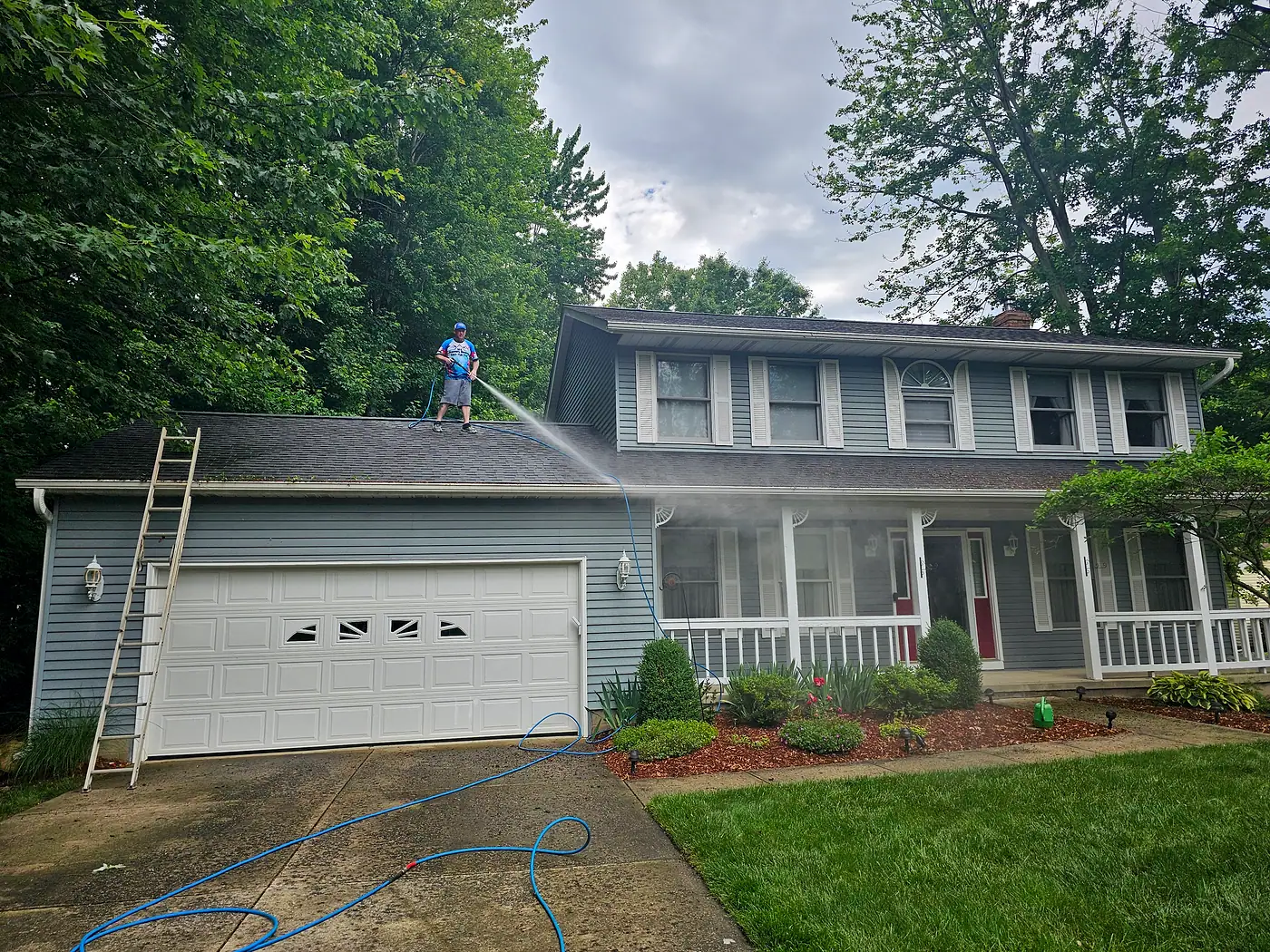 Ladder against the garage while a worker cleans the roofline of a two-story house