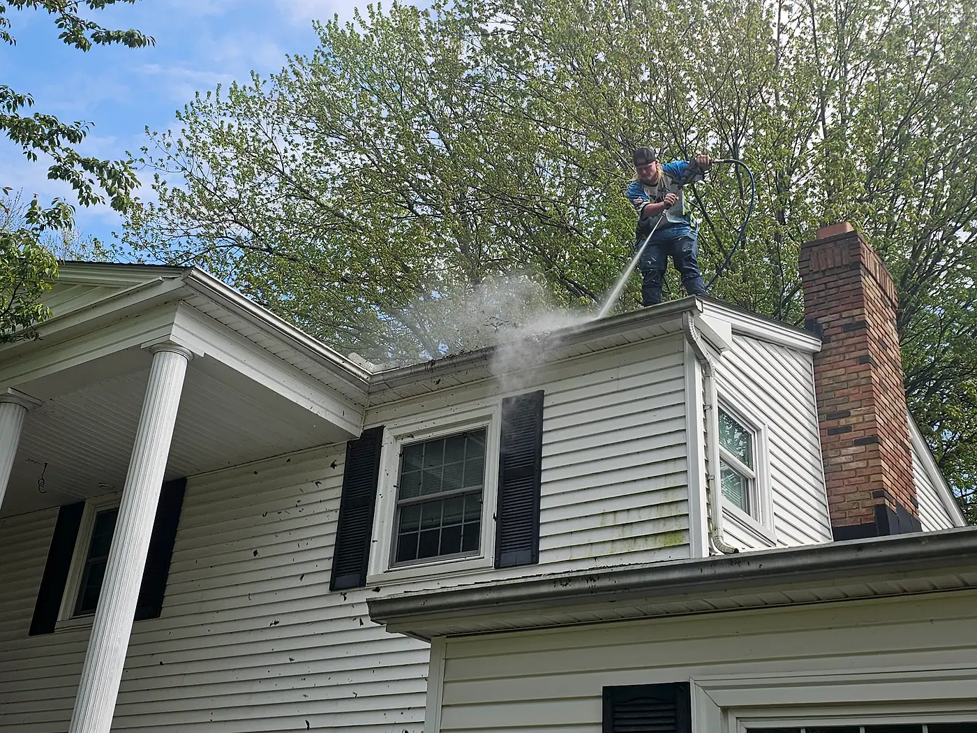 Worker cleaning the roofline of a house with a brick chimney