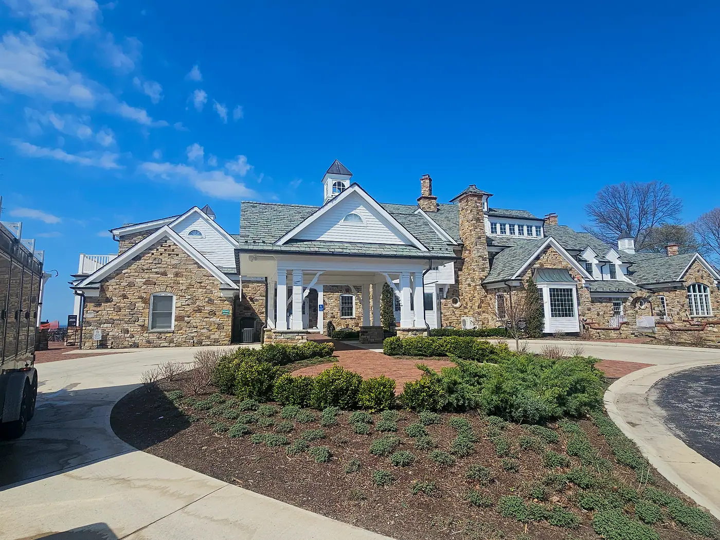 Stone and white cottage-style home with a landscaped garden bed after a house wash