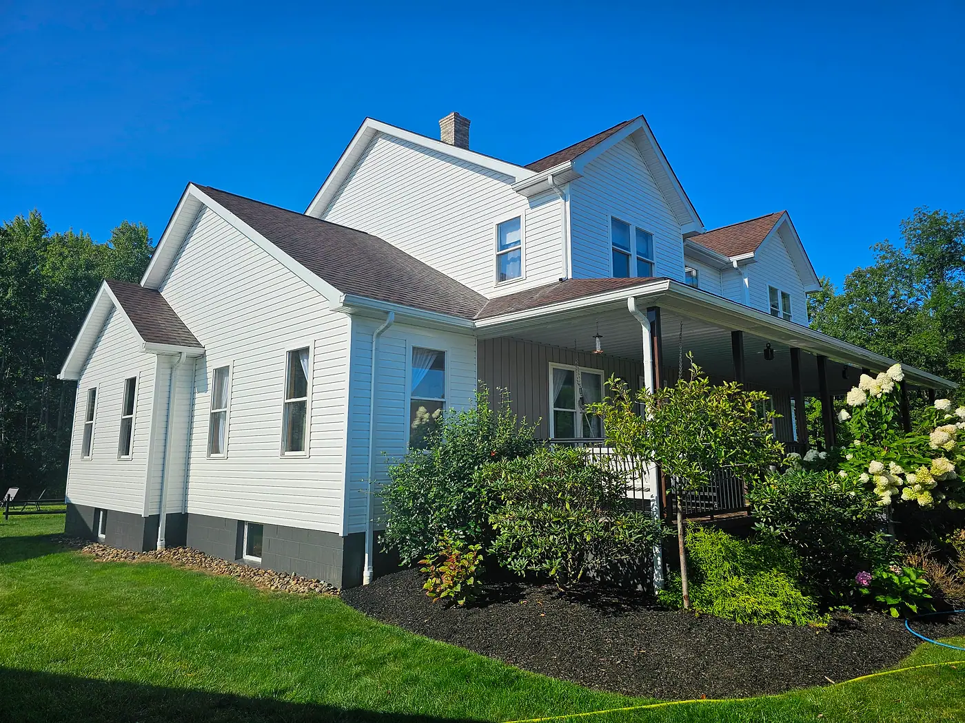 Freshly washed white farmhouse with a covered porch and flowering garden