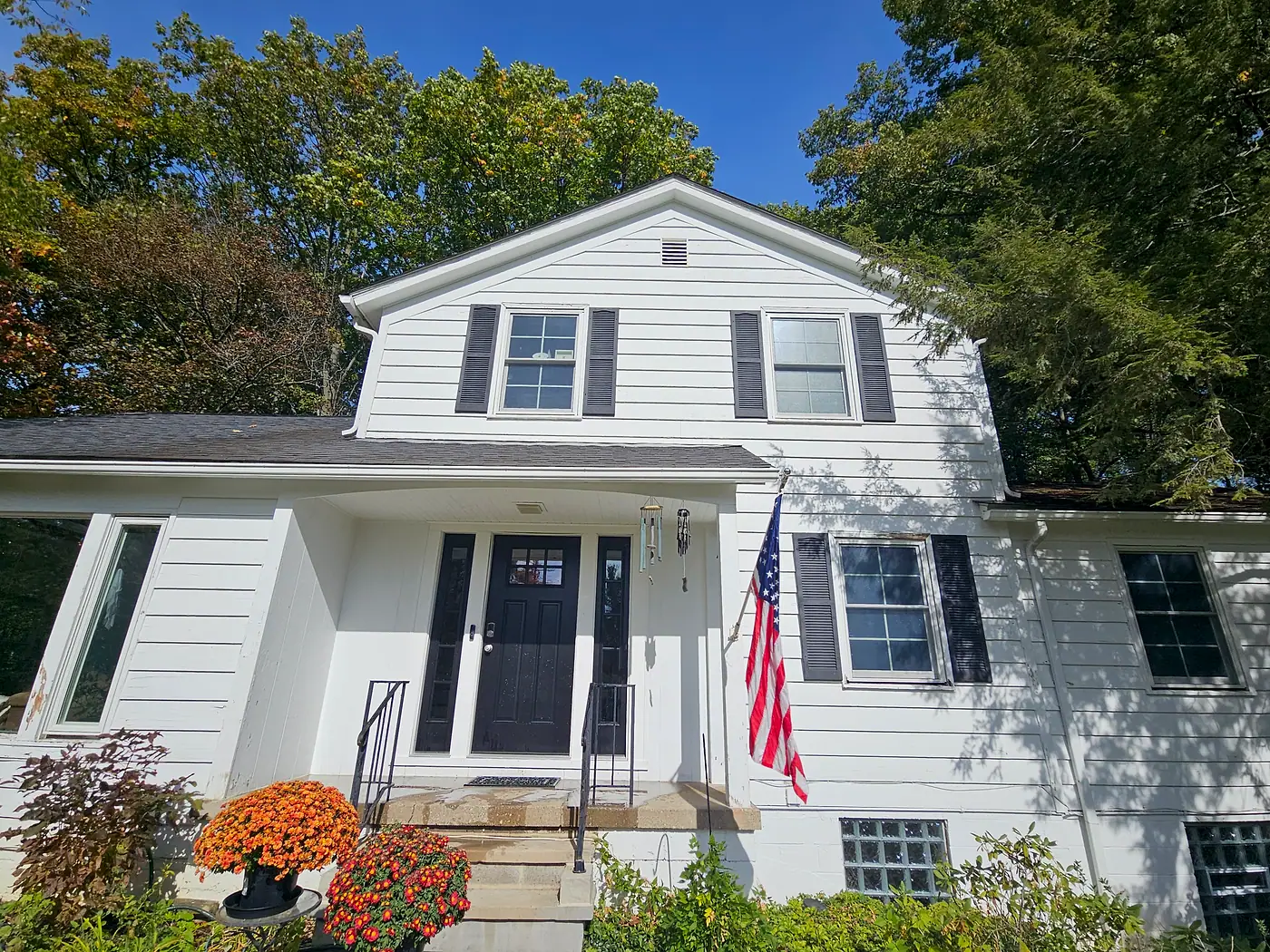 Clean white house with black shutters, an American flag, and fall mums by the front door