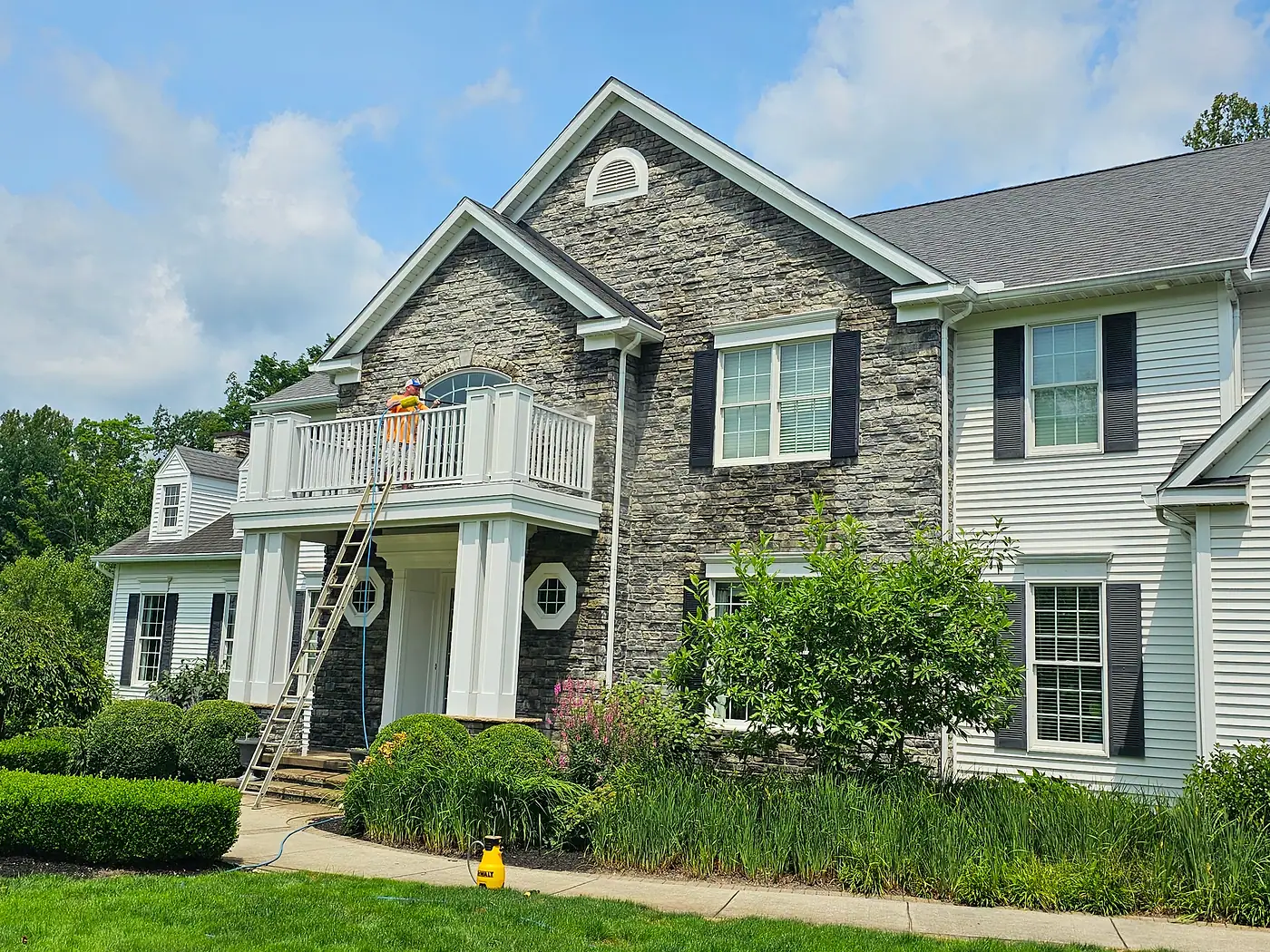 Stone-front two-story house with a balcony and a ladder against the washed siding