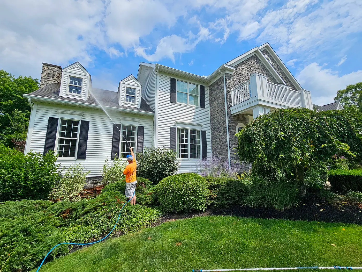 Worker washing a two-story white house with dormer windows
