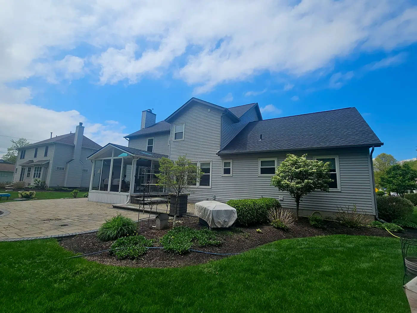 Blue-gray two-story house with a sunroom and a rock garden under a partly cloudy sky