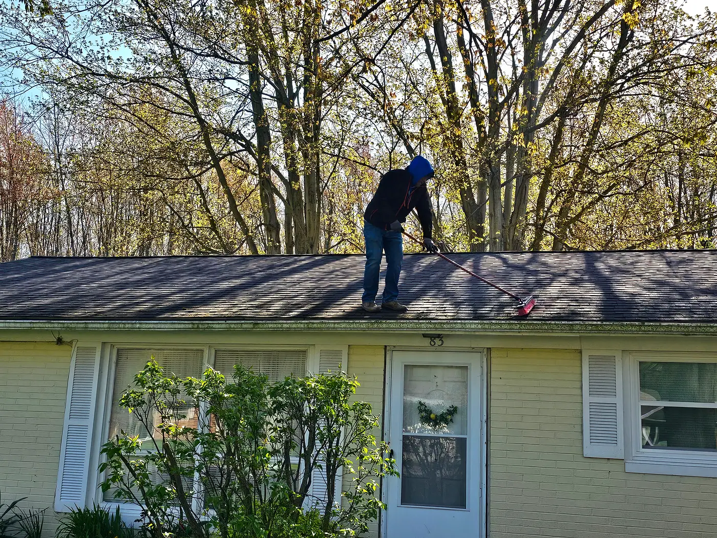 Worker soft washing the roof of a single-story house