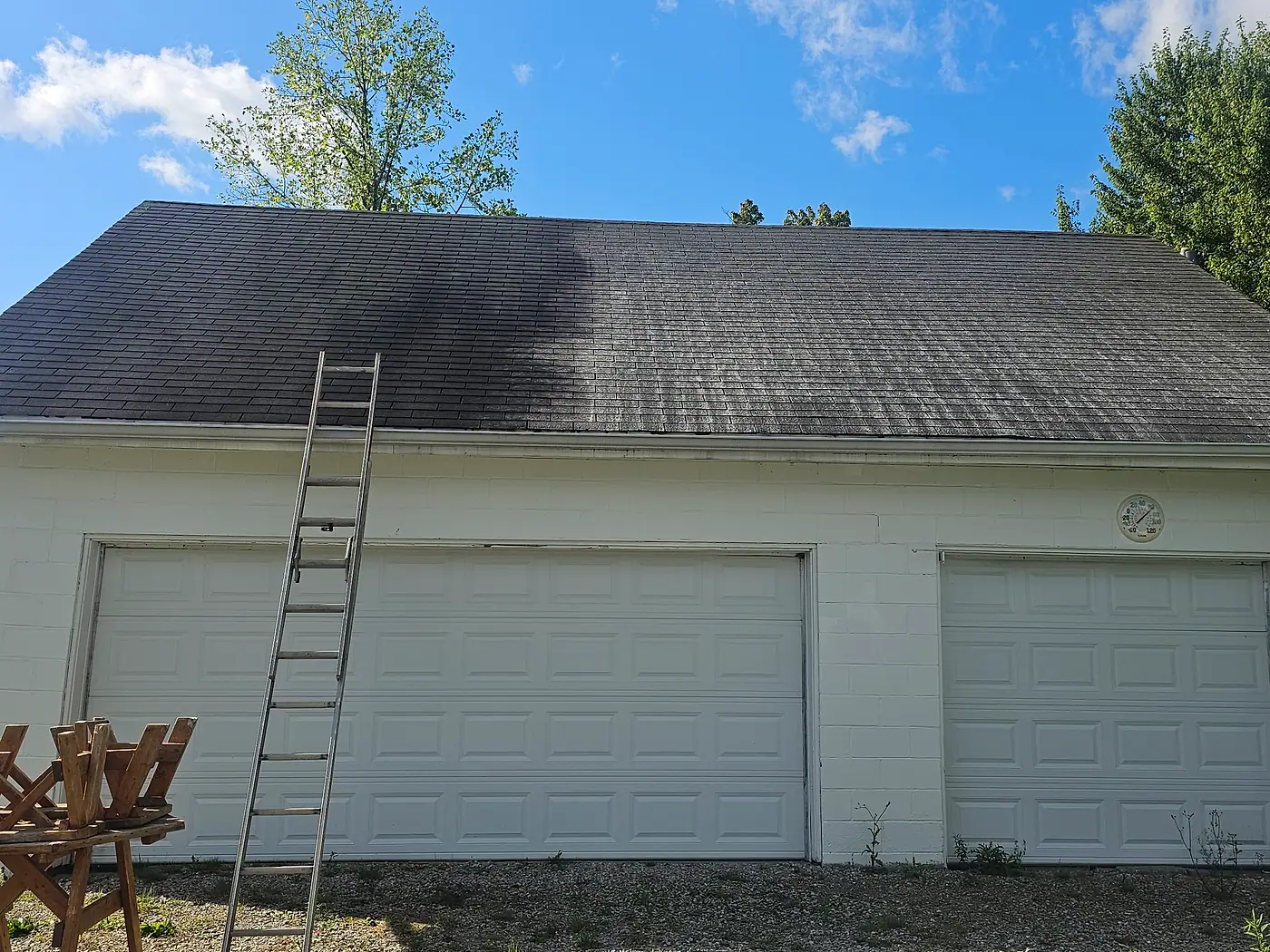 Detached garage with a black-streaked roof and a ladder ready for roof cleaning