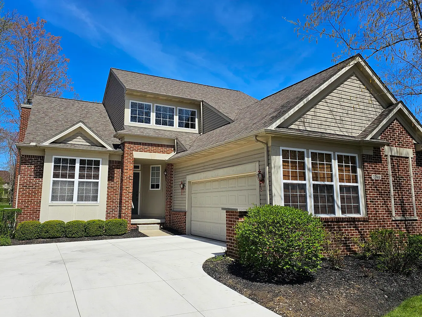 Tan brick and siding home with a bay window and a clean driveway
