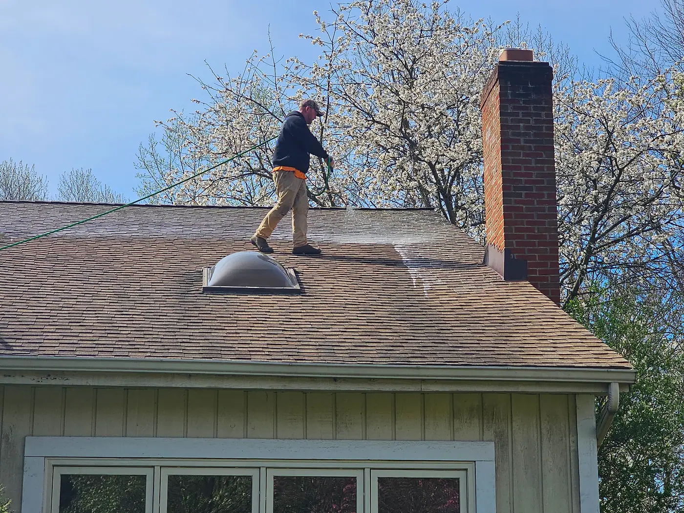Worker on a shingle roof beside a brick chimney and skylight