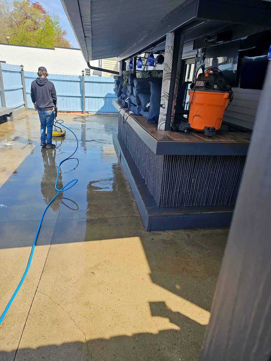 Crew member cleaning a concrete patio with a surface cleaner beside a covered bar area in Eastlake