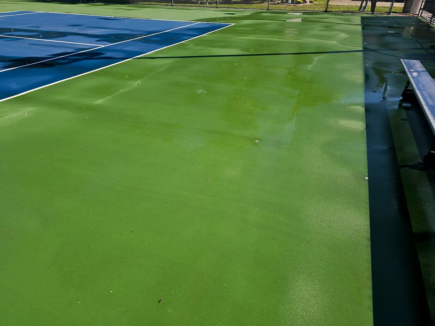 Green and blue tennis courts with a bench, wet from cleaning, at Geneva High School