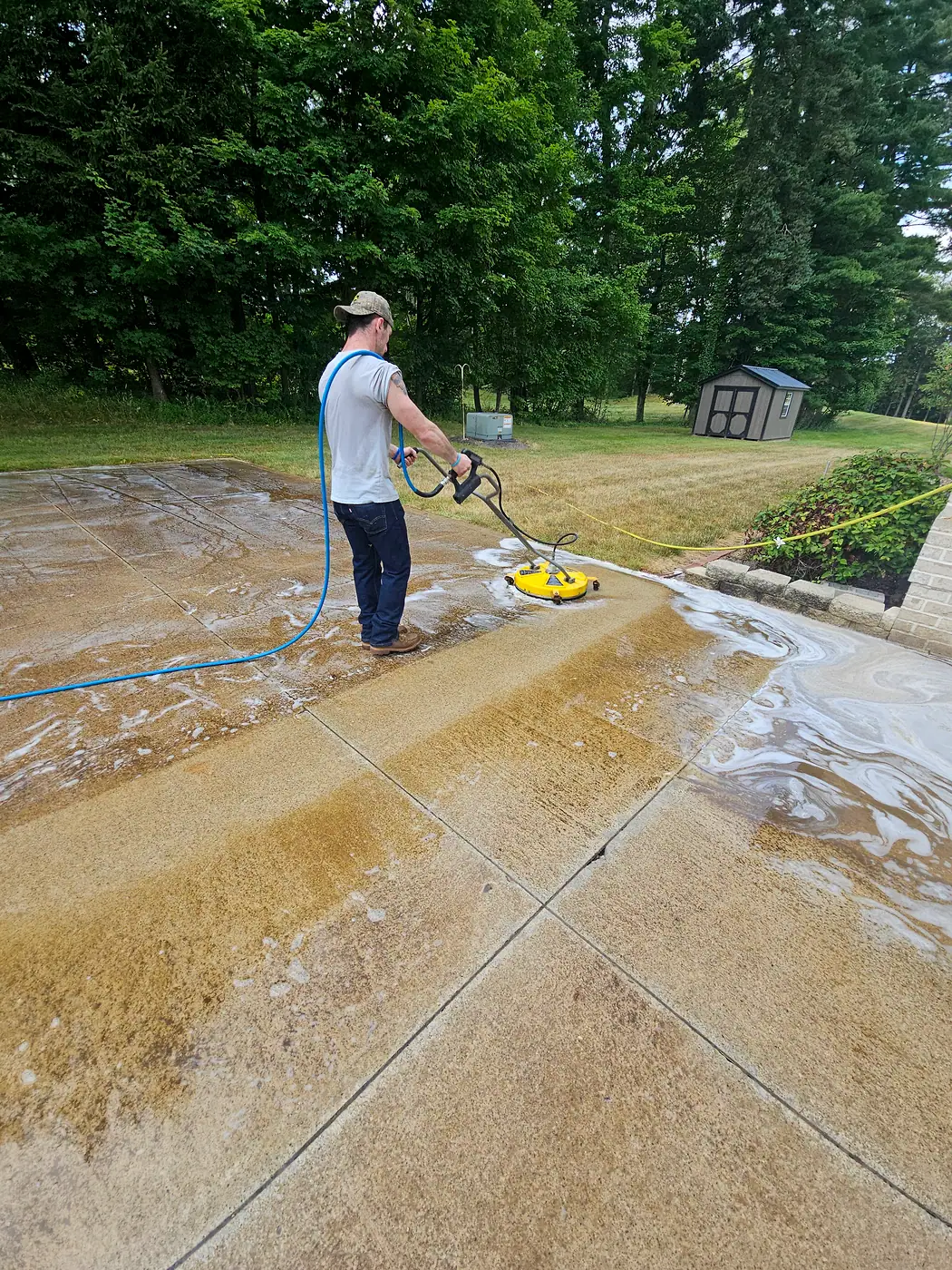 Crew member cleaning a concrete driveway with a yellow surface cleaner in Willoughby, half of it already clean